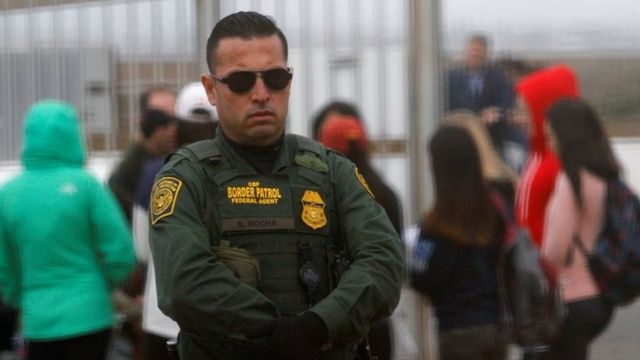 A US Border Patrol agent looks on at people along the US-Mexican border.