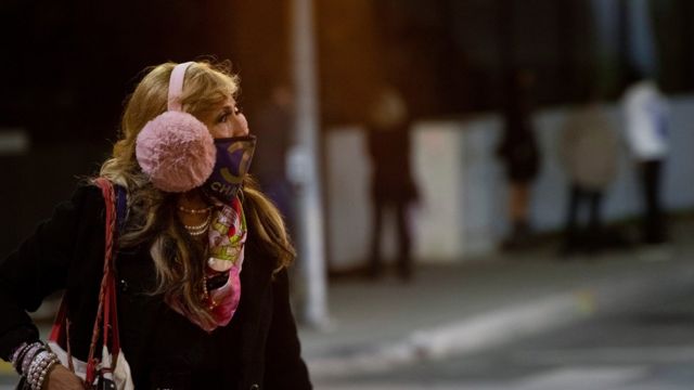 A woman wearing a protective face mask and earmuffs crosses the street during the outbreak of the coronavirus disease) in Beverly Hills, California, US, November 20, 2020