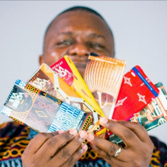 Un homme tenant une variété de chocolat de la marque “NYA MBOA” qui signifie “Le chocolat de chez-nous"marque 
