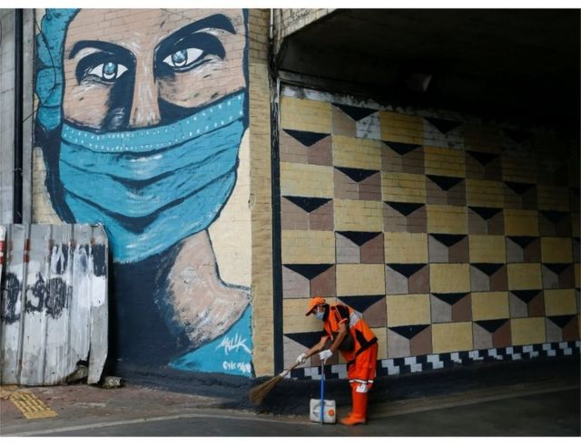 A worker wearing a protective face mask sweeps the street near a mural promoting awareness of the coronavirus disease (COVID-19) outbreak in Jakarta, Indonesia, October 2, 2020.