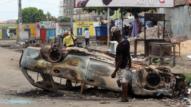 A man stands next to a burnt out car after a protest in Kinshasa, Democratic Republic of Congo, Monday, Sept. 19, 2016