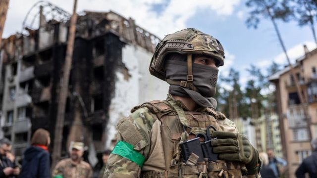 Um soldado ucraniano em frente a um prédio destruído.