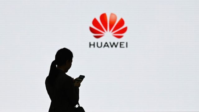 A Huawei logo is seen on the background as a staff member uses her mobile phone