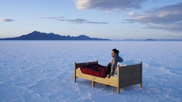 Hombre despertando sobre una cama aislada en paisaje frío.