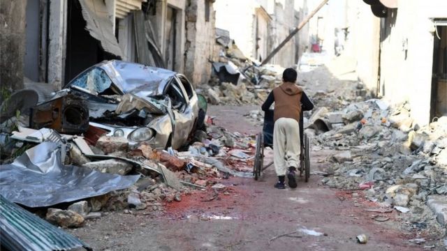 A boy pushes a wheelchair along a damaged street in the east Aleppo neighbourhood of al-Mashatiyeh, Syria, in this handout picture provided by UNHCR on 4 January 2017