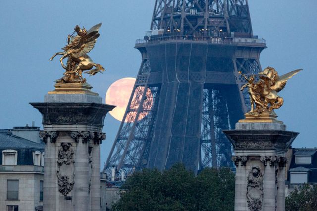 The pink supermoon seen against the Eiffel Tower and the Pegasus Held By Fame statues on the Pont Alexandre III bridge in Paris, France