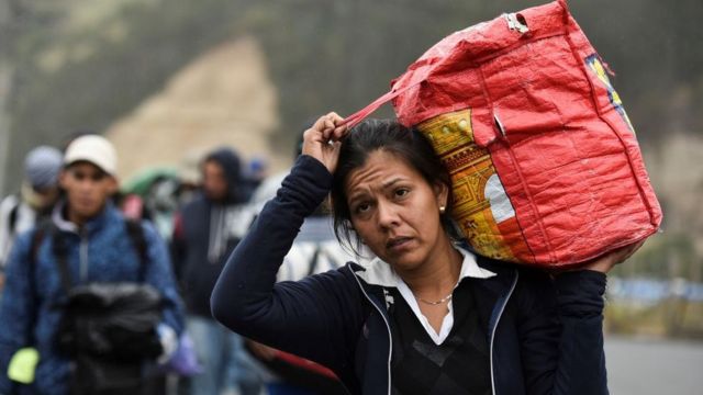 A Venezuelan immigrant carries his suitcase over his shoulder.