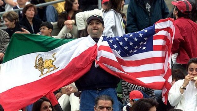 A man holds up the flags of Iran (the flag in use up to the revolution of 1979) and the United States at the 2000 friendly match between the nations
