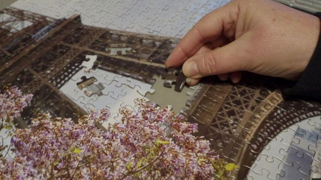 Close em uma mão terminando de montar um quebra-cabeça da Torre Eiffel