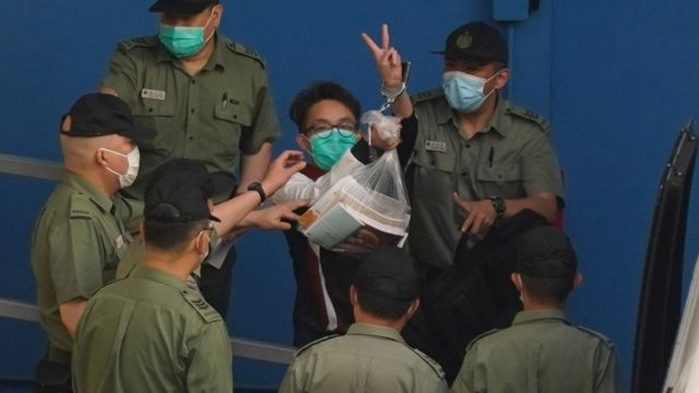 被鎖上手銬的陳皓桓在獄警押送下向九龍荔枝角收押所外記者舉起勝利手勢（28/5/2021）