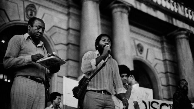 Antonio Leite, Milton Barbosa (ao microfone) e Flavio Carrança durante o primeiro ato público do MNU, nas escadarias do Teatro Municipal de São Paulo, em 7 de julho de 1978