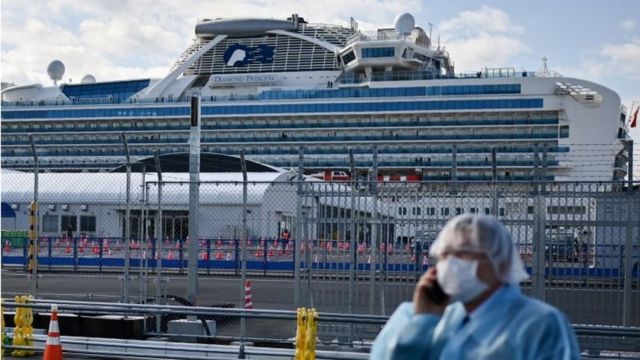 A man in protective gear speaks on the phone near the Diamond Princess cruise ship in quarantine due to fears of the new COVID-19 coronavirus, at the Daikoku Pier Cruise Terminal in Yokohama on February 19, 2020