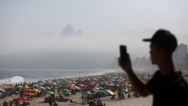 Young man points his cell phone at Ipanema beach, taking a photo