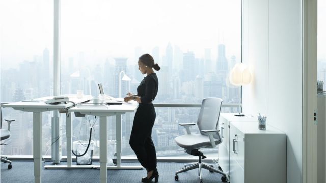 Mulher trabalhando em pé usando mesa com altura regulável