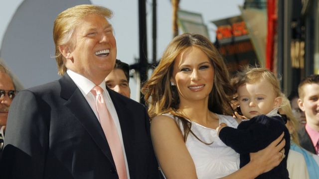 Trump ao lado de Melania, que segura bebê no colo; o casal sorri