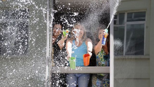 Três pessoas jogam água pela janela