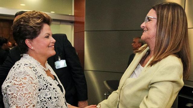 Dilma e Graça Foster sorrindo enquanto se cumprimentam com as mãos 