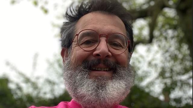 A close up selfie of Charles wearing a pink fundraising t-shirt, he has red glasses and a bushy grey beard