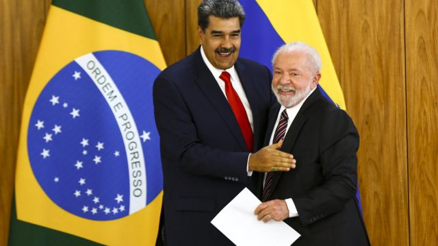 O presidente da Venezuela, Nicolás Maduro, com o presidente Lula. Os dois estão de terno, abraçados e sorrindo. Lula leva um papel na mão