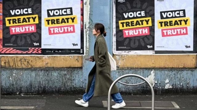 mulher andando em frente a cartaz de campanha