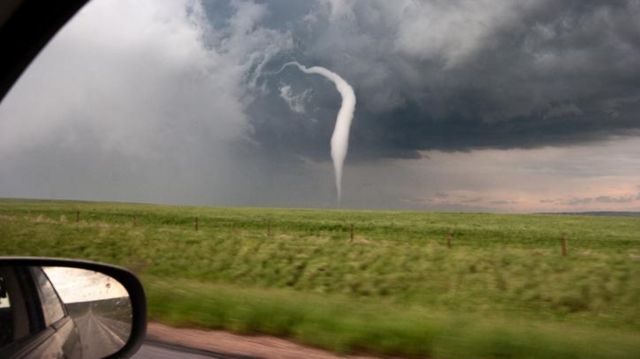 Foto tirada de dentro de carro mostra tornado ao fundo