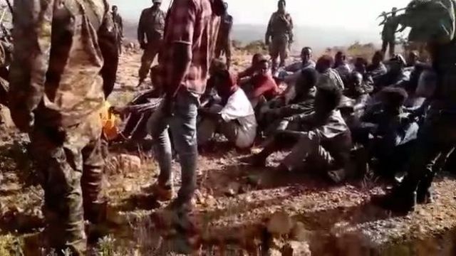 The video shows a group of men in civilian clothes sitting on the ground before the slaughter