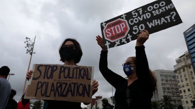 Duas mulheres, de máscara, seguram cartazes críticos a Bolsonaro em manifestação na rua