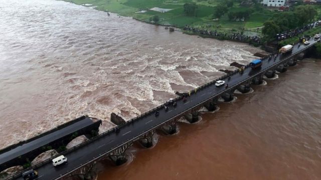 In this photograph released by The Indian Coast Guard on August 3, 2016, bystanders look at the partially collapsed bridge over the River Savitri in Raigad District some 100kms from Mumbai