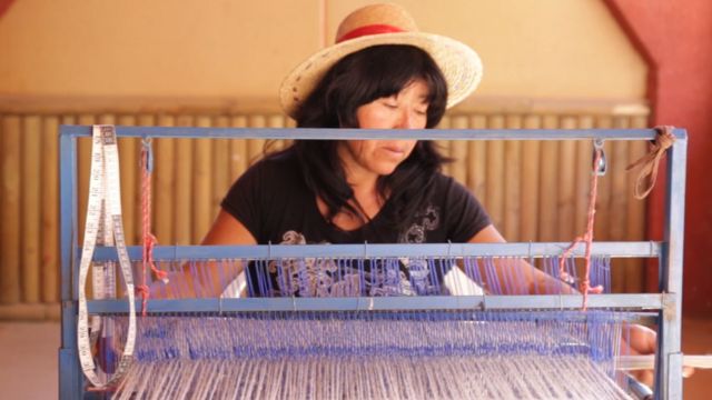 Una mujer aymara teje en el telar.