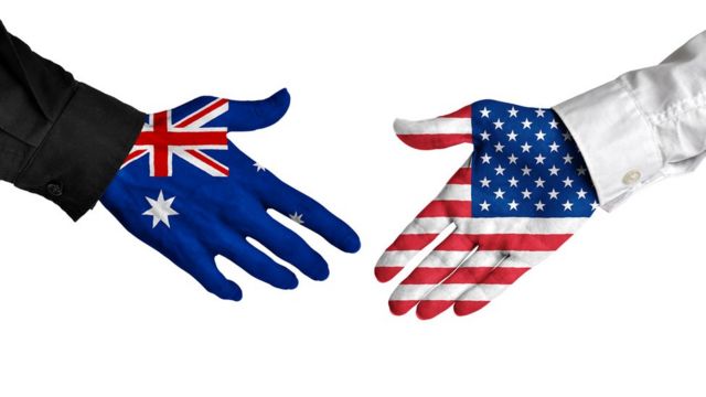 A stock image of a hand painted with an Australian flag reaching out to hand with an American flag