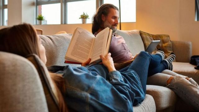 A man and a woman sit on a couch reading