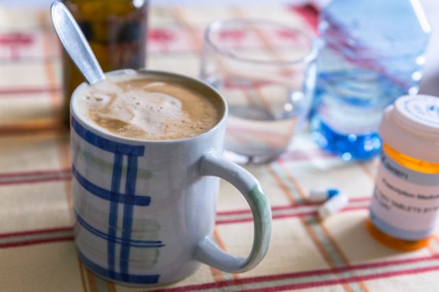 Xícara de café com leite ao lado de um comprimido sobre uma mesa