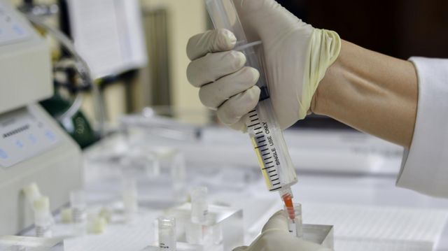 Mão de médico com luva colocando células-tronco em uma seringa em laboratório