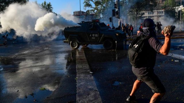 Homem arremessa objeto na rua em manifestação, com camburão atrás