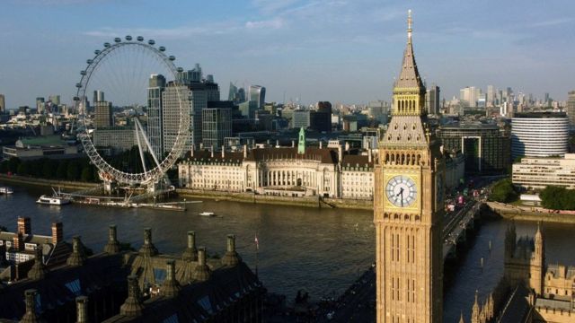 Foto colorida mostra vista de Londres: o Big Ben e a roda gigantes, sob um céu azul poluído