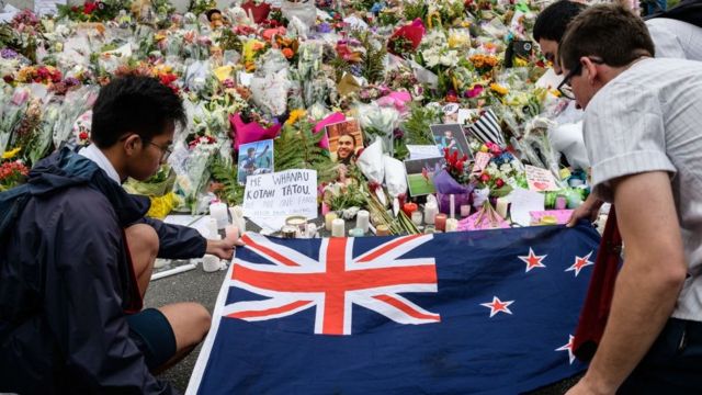 Citizens place a New Zealand flag next to flowers to commemorate the victims of the Christchurch shootings in 2019