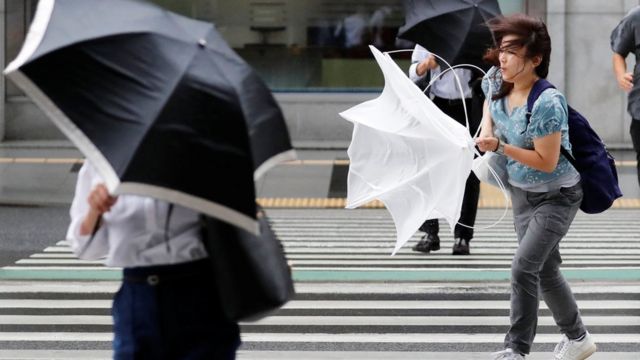Жінка з парасолькою, яку вивернув вітер, на пішохідному переході