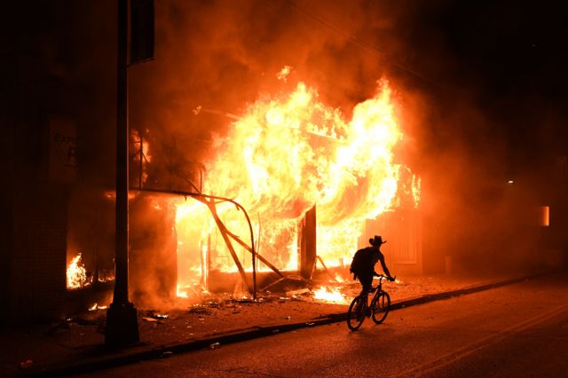 1. A man on a bicycle rides past a burning building during the civil unrest in Minneapolis, Minnesota, resulting from the killing of an unarmed black man by a police officer .Demonstrators near Minneapolis' US Bank Stadium during protests resulting from the killing of an unarmed black man, George Floyd, by police.