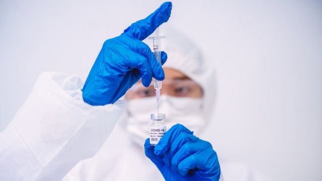 Profissional de saúde paramentado segura uma ampola e uma seringa de vacina contra a covid-19