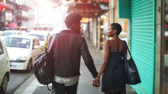 A man and a woman walk away from the camera down a city street