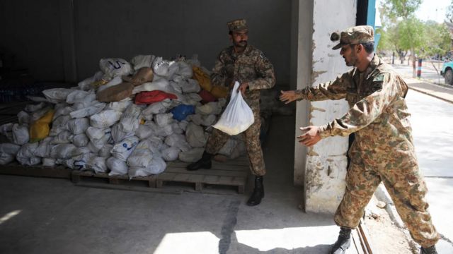 Militares em roupa camuflada em tons de bege manuseando doações em sacolas plásticas