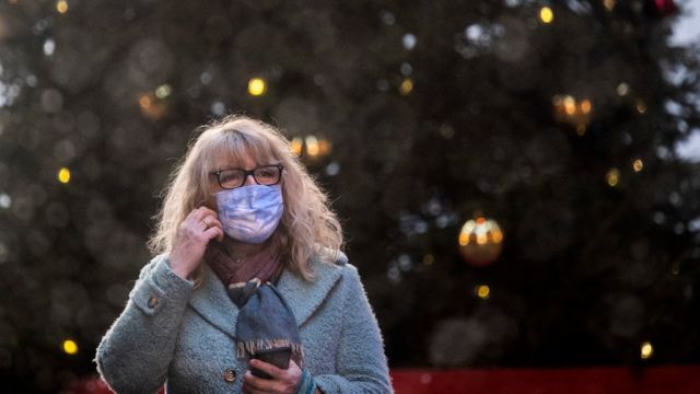 Uma mulher usando uma máscara em frente a uma árvore de Natal em Londres