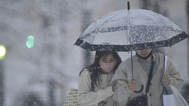 Imagem de uma casal japonês dividindo um guarda-chuva na chuva