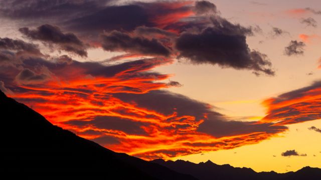 Bright red and orange clouds, over some dark mountains