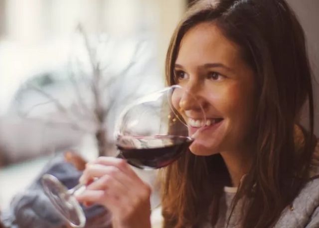 Une femme en sourire tenant un verre de vin.