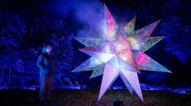 Em foto noturna, mulher aparece perto de grande estrela decorativa iluminada