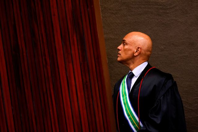 Alexandre de Moraes olhando de lado prximo a cortina vermelha