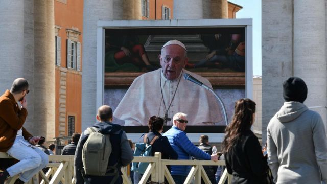 {eople watch a screen live-broadcasting Pope Francis's Sunday Angelus prayer in St. Peter' s Square at the Vatican