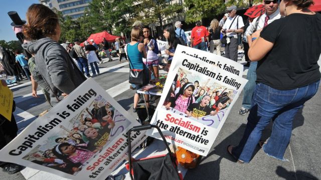 Pessoas protestam segurando cartazes contra o capitalismo