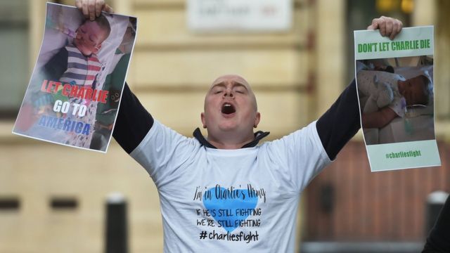 Hombre protestando frente a los tribunales con carteles que dicen: "Dejen a Charlie ir a Estados Unidos".